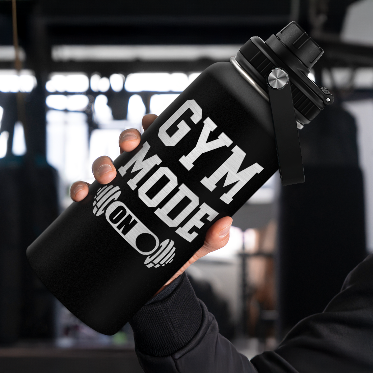 Black water bottle with 'GYM MODE ON' text held by a person in a blurred indoor setting
