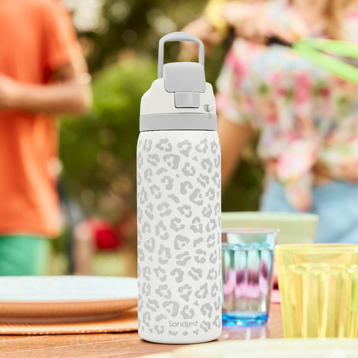 Leopard print water bottle on a table with people and outdoor setting in the background