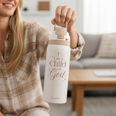 Person holding a white water bottle with 'I am a Child of God' text in a living room setting.
