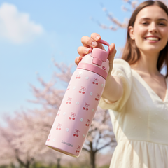 Woman holding a pink water bottle with cherry design outdoors