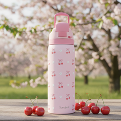 Pink water bottle with cherry design on a wooden table with cherry berries, against a blurred cherry blossom background.