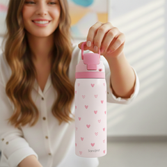 Woman holding a pink water bottle with heart patterns, brand 'Sandjess' visible
