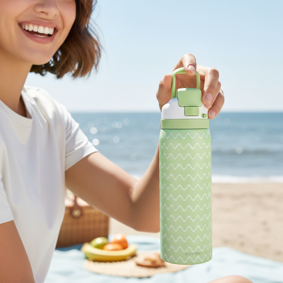 Person holding a green water bottle with a beach in the background