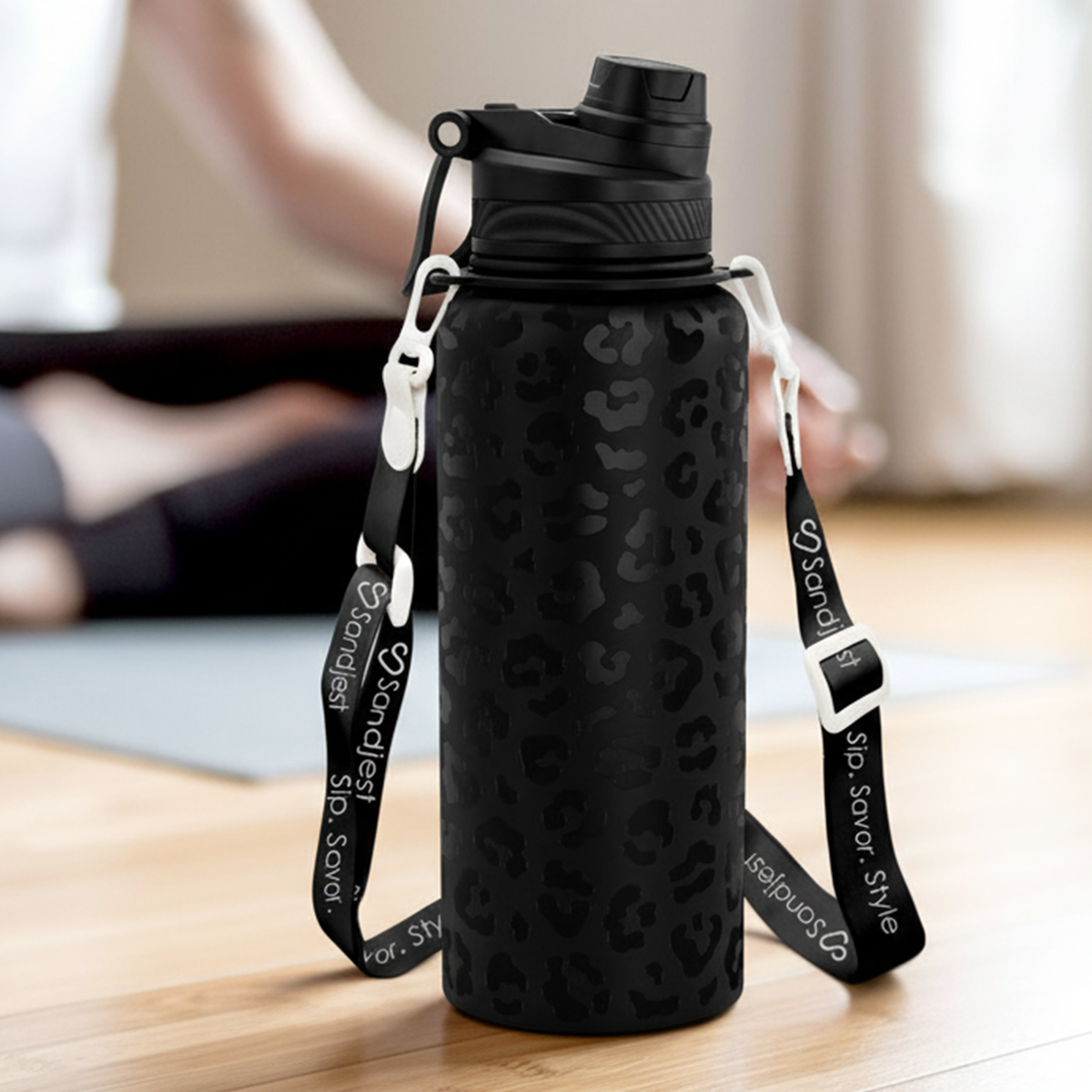 Black water bottle with leopard print pattern and strap on a wooden floor.