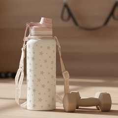 White water bottle with star pattern and pink lid on a wooden surface, with dumbbells in the background.