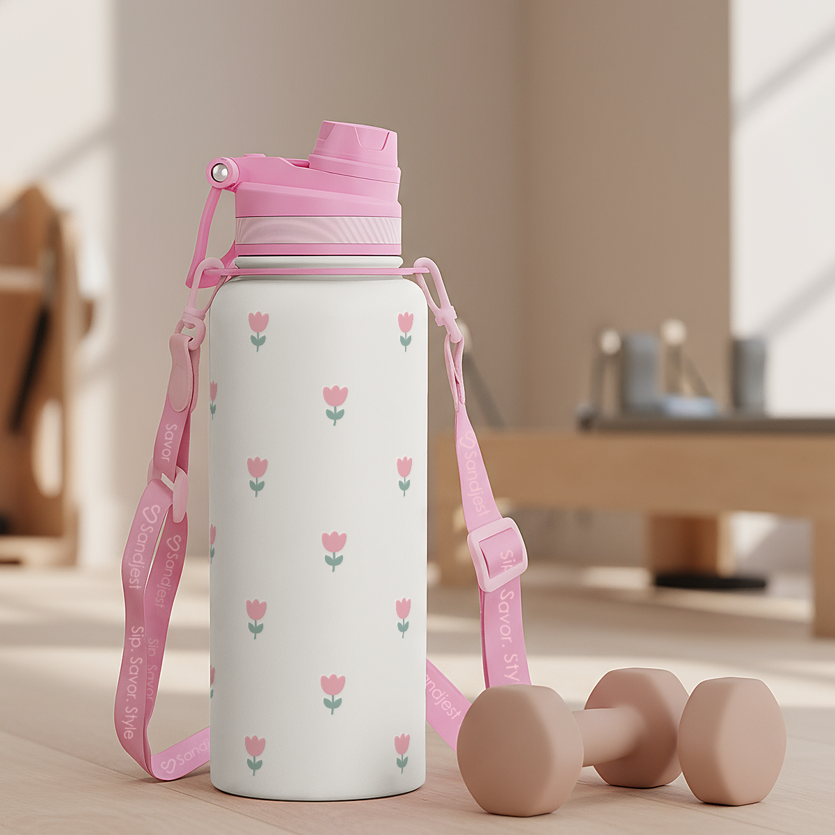 White water bottle with pink floral design and pink lid and strap on a wooden floor.