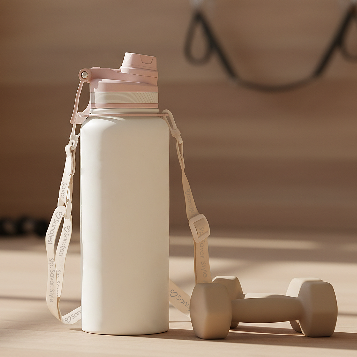 White water bottle with pink cap and strap, accompanied by small wooden dumbbells on a wooden surface.