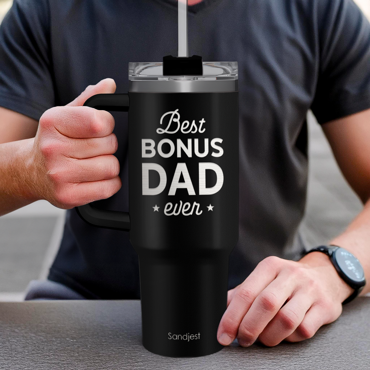 Person holding a black mug with 'Best Bonus Dad ever' text, wearing a dark shirt.