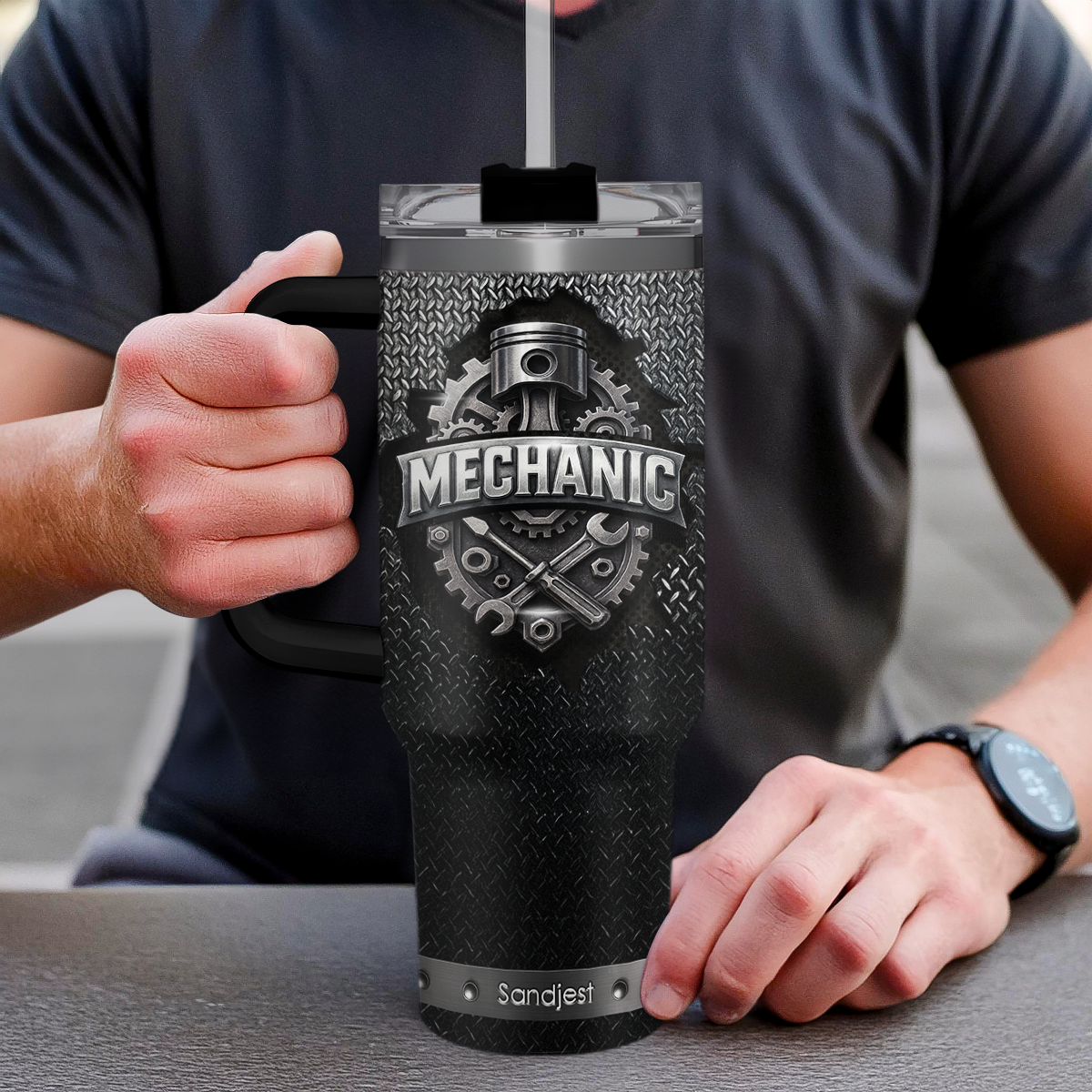 Person holding a black tumbler with 'Mechanic' design and 'Sandjast' branding.