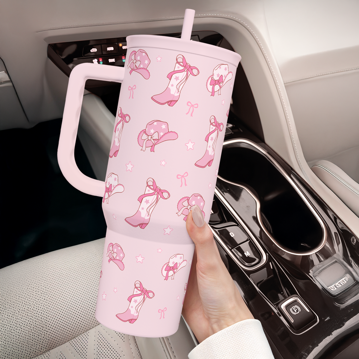 Pink tumbler with decorative patterns held by a hand in a car.