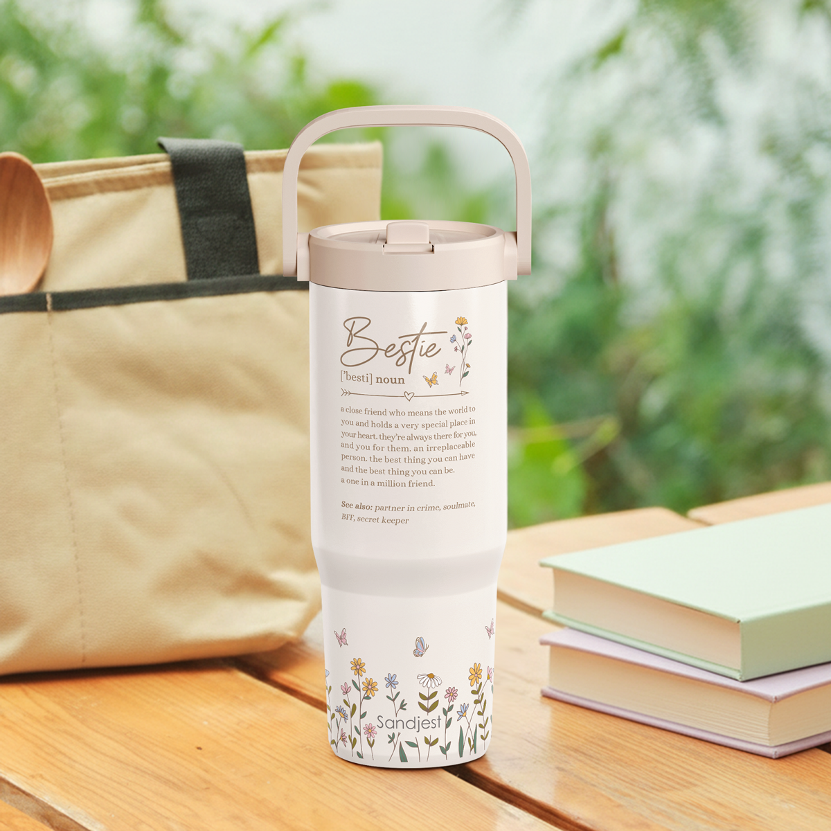 Tumbler with floral design and text on a wooden surface with books and a bag in the background