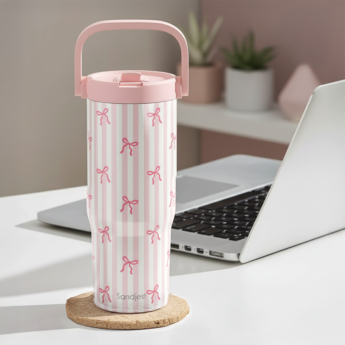 White tumbler with pink bow pattern on a desk with a laptop
